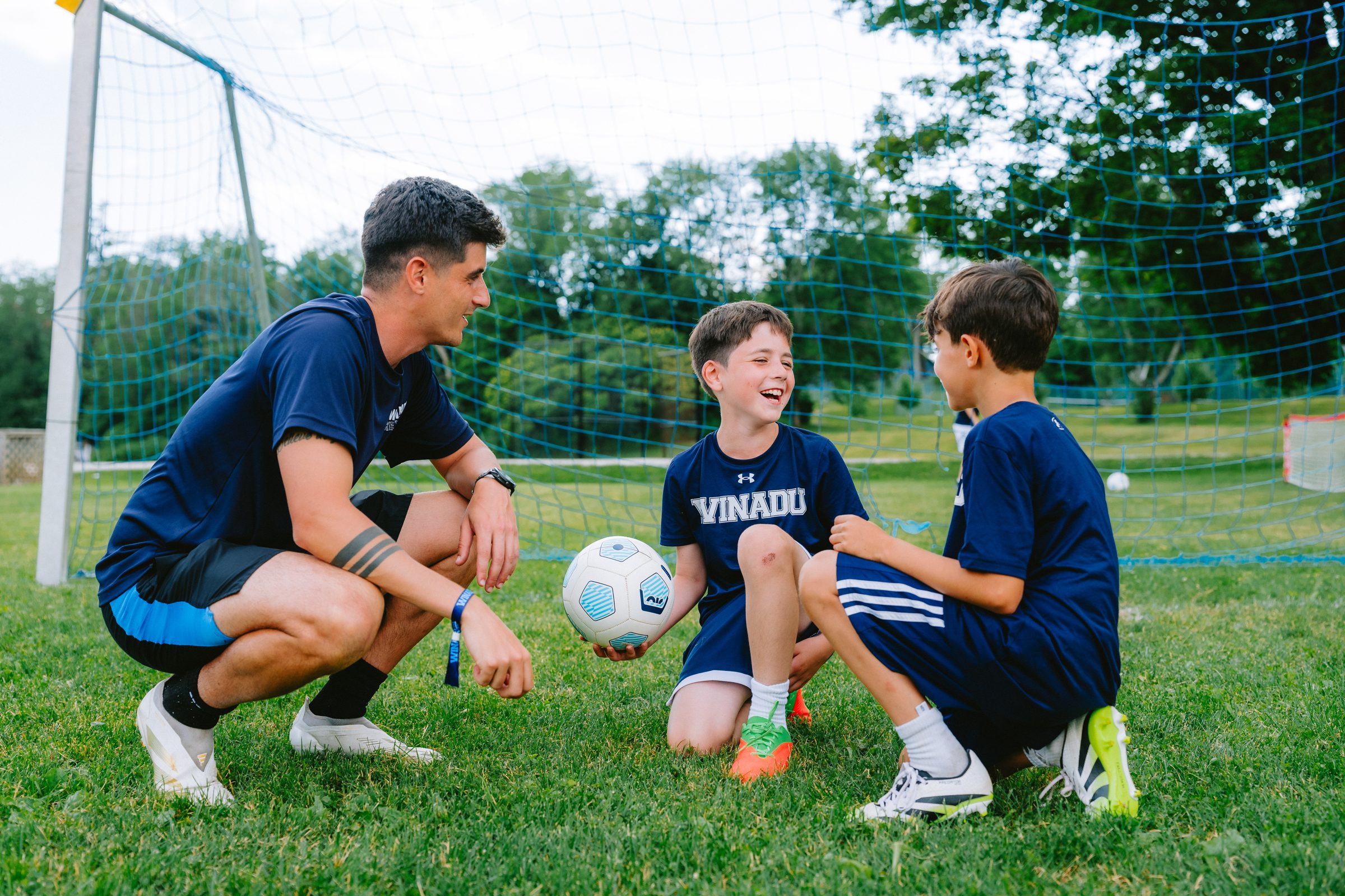Camp Winadu soccer coach kneeling with two campers